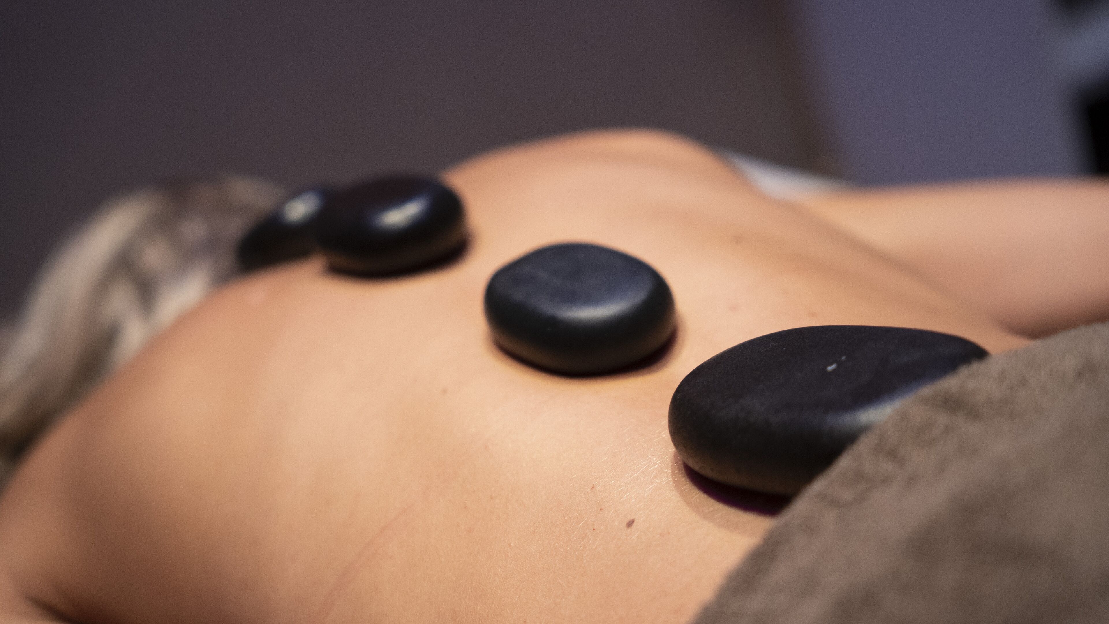 A person lying down with three black stones placed on their back.