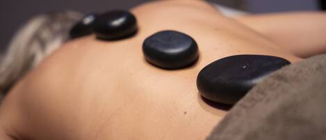 A person lying down with three black stones placed on their back.