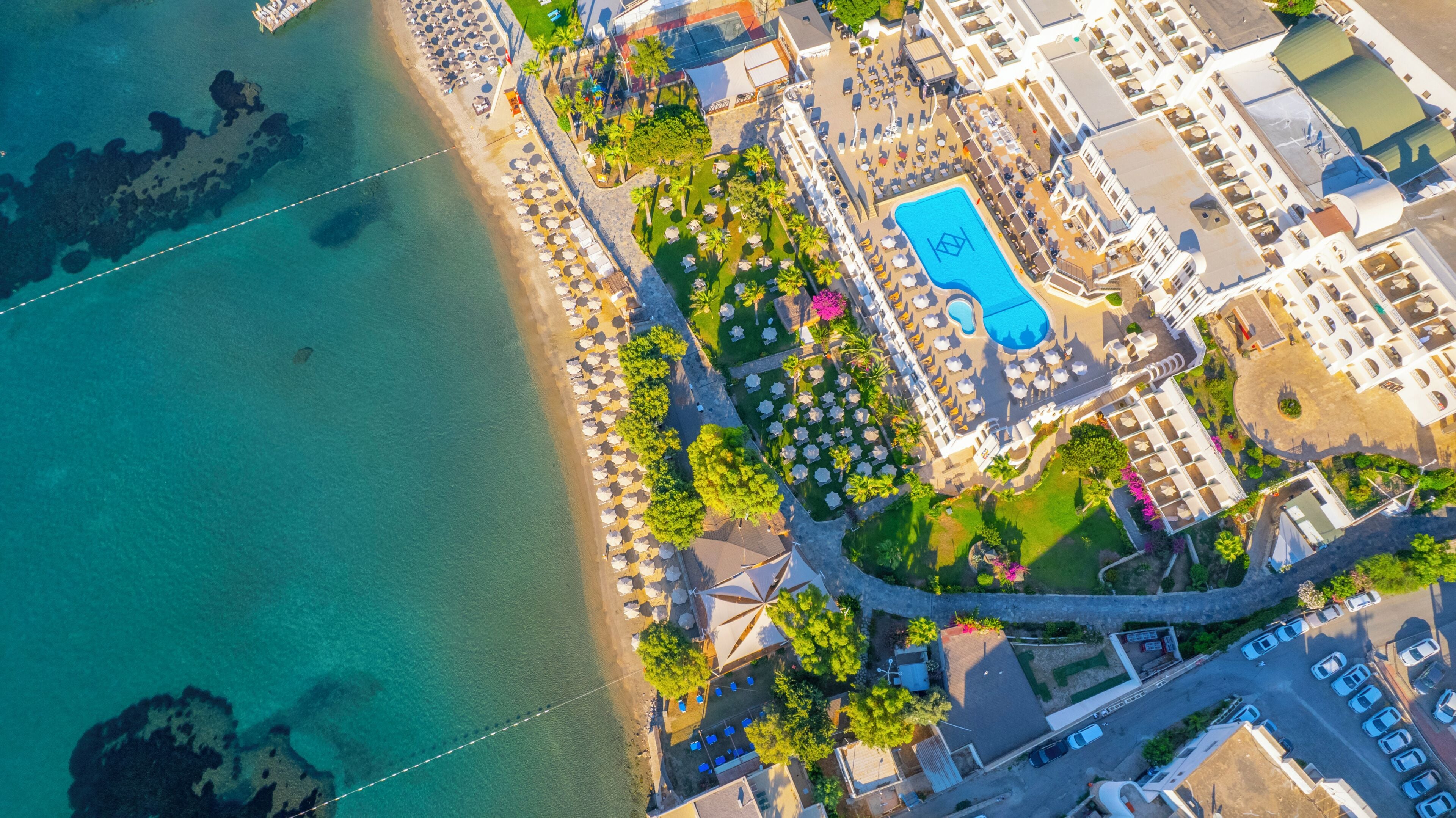 Eine Vogelperspektive zeigt einen Ferienort mit Pool, Strand und mehreren Gebäuden.
