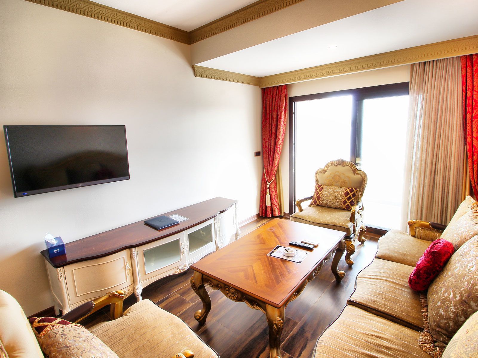 A hotel room with a flat-screen TV, a wooden coffee table, a sofa, and a chair.