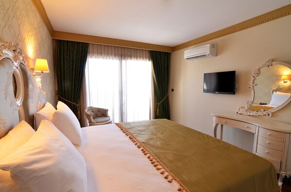 A hotel room with a large bed, a dresser, a television, and a mirror. - Azka Hotel (Bodrum)