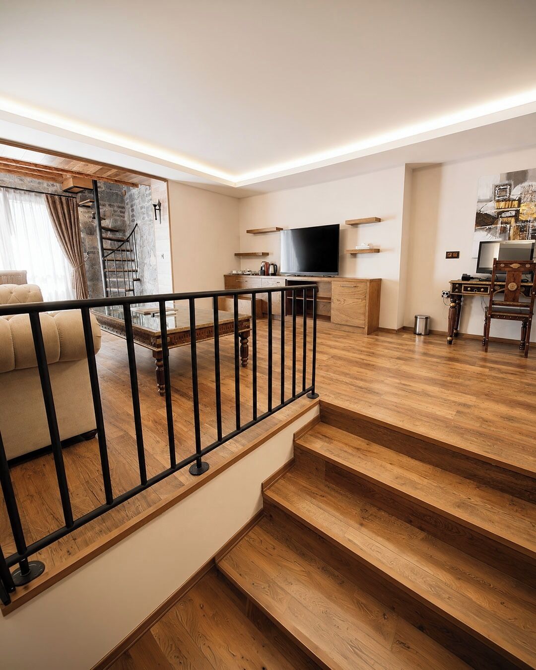 A modern living room with a staircase, a sofa, a TV, and a desk with a computer.