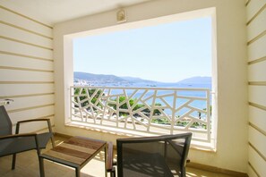 A balcony with a view of the sea and mountains, furnished with two chairs and a small table.