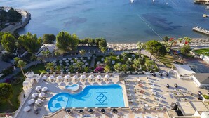 Un resort con una piscina grande, tumbonas y vistas al mar.