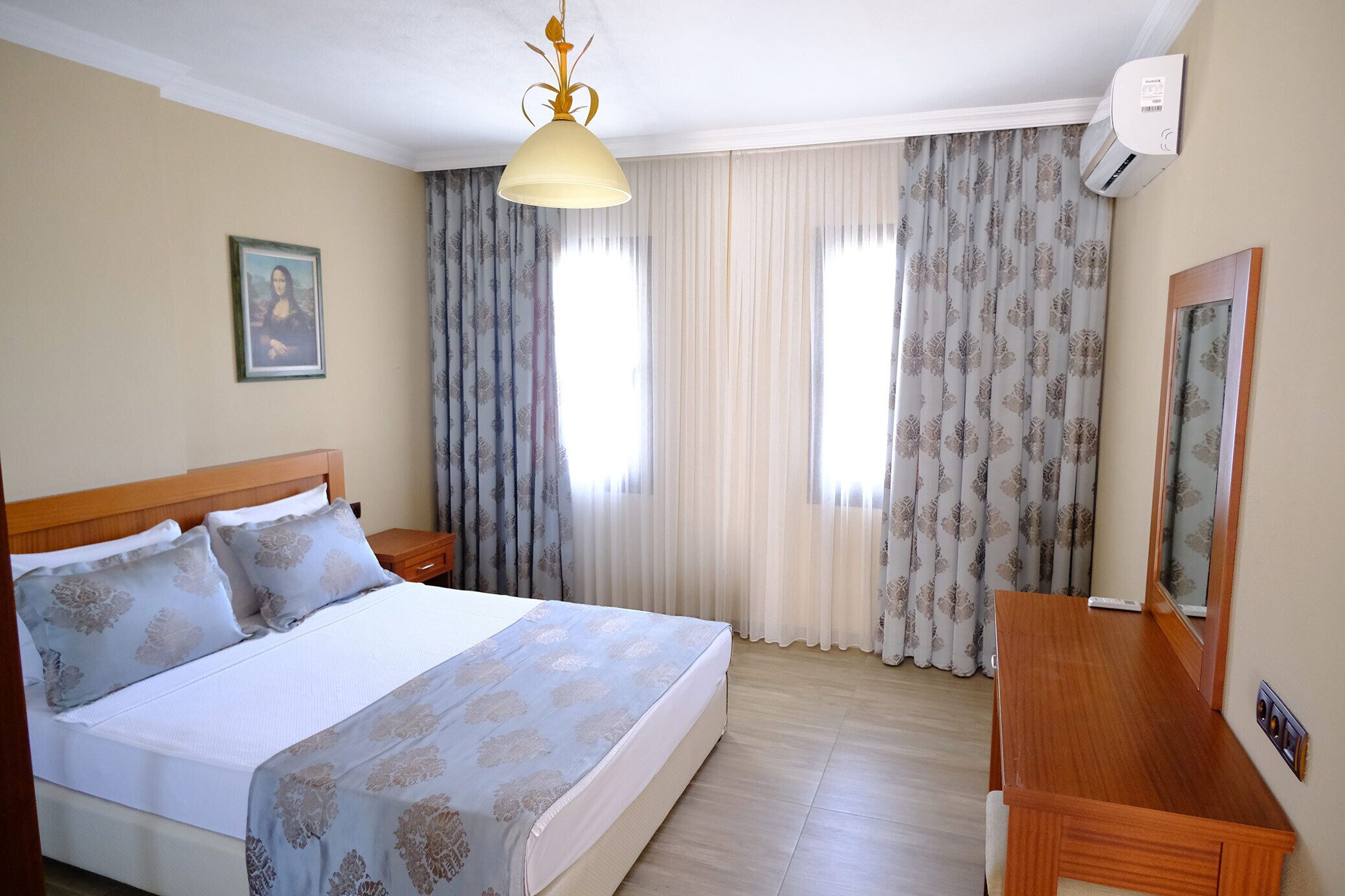 Una habitación de hotel con cama, mesitas de noche, un escritorio y un espejo.