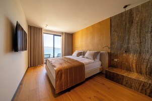 Un dormitorio moderno con una cama grande, suelo de madera, una pared de acento de piedra y un televisor montado en la pared.