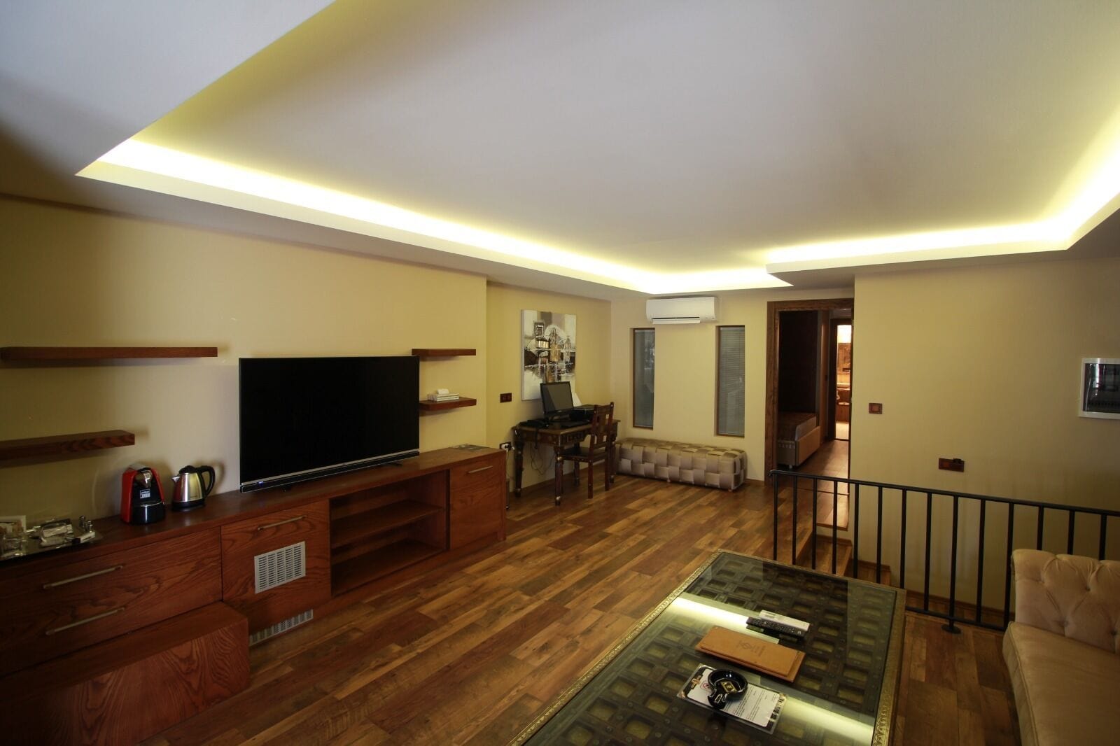 A living room with a flat-screen TV, wooden entertainment unit, and a glass coffee table.