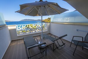 Un balcon avec une table et des chaises, un grand parasol et une vue sur la mer et les collines.
