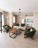 Una sala de estar moderna con un sofá, dos sillones, una mesita de centro y una cocina al fondo.