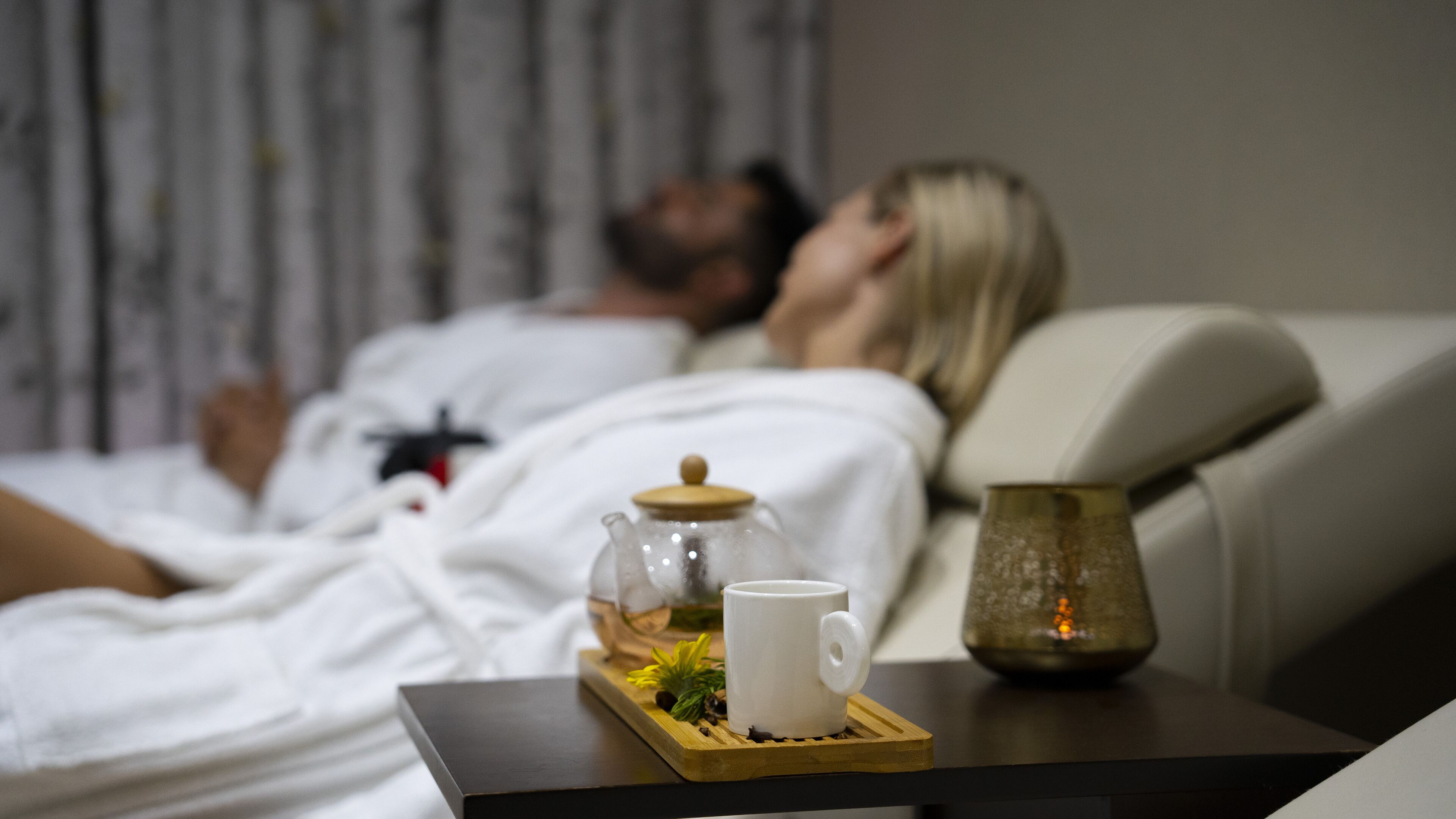 A person lying on a bed in a room with a coffee table in the foreground.