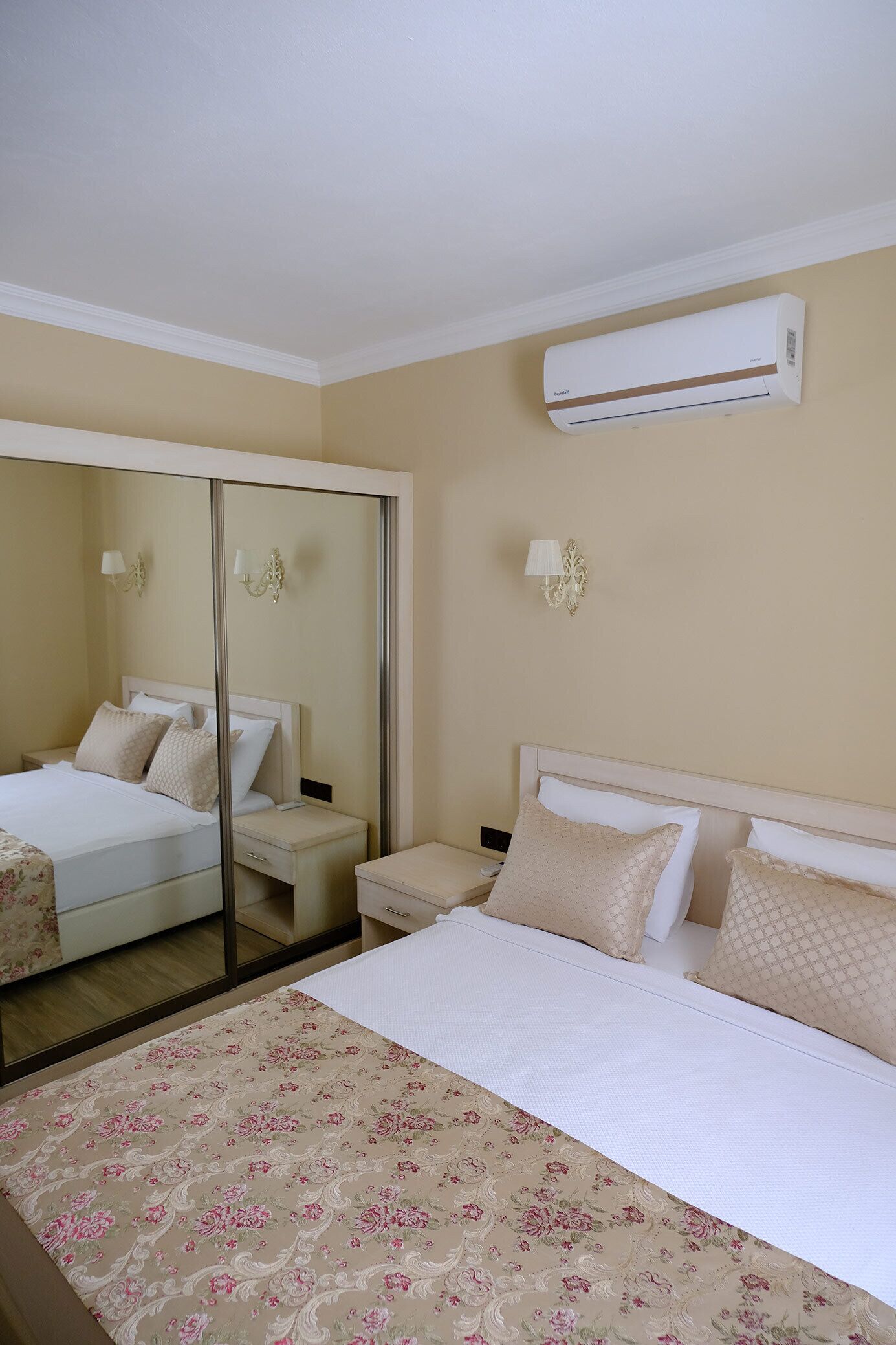 Una habitación de hotel con cama, mesita de noche, espejo y aire acondicionado.
