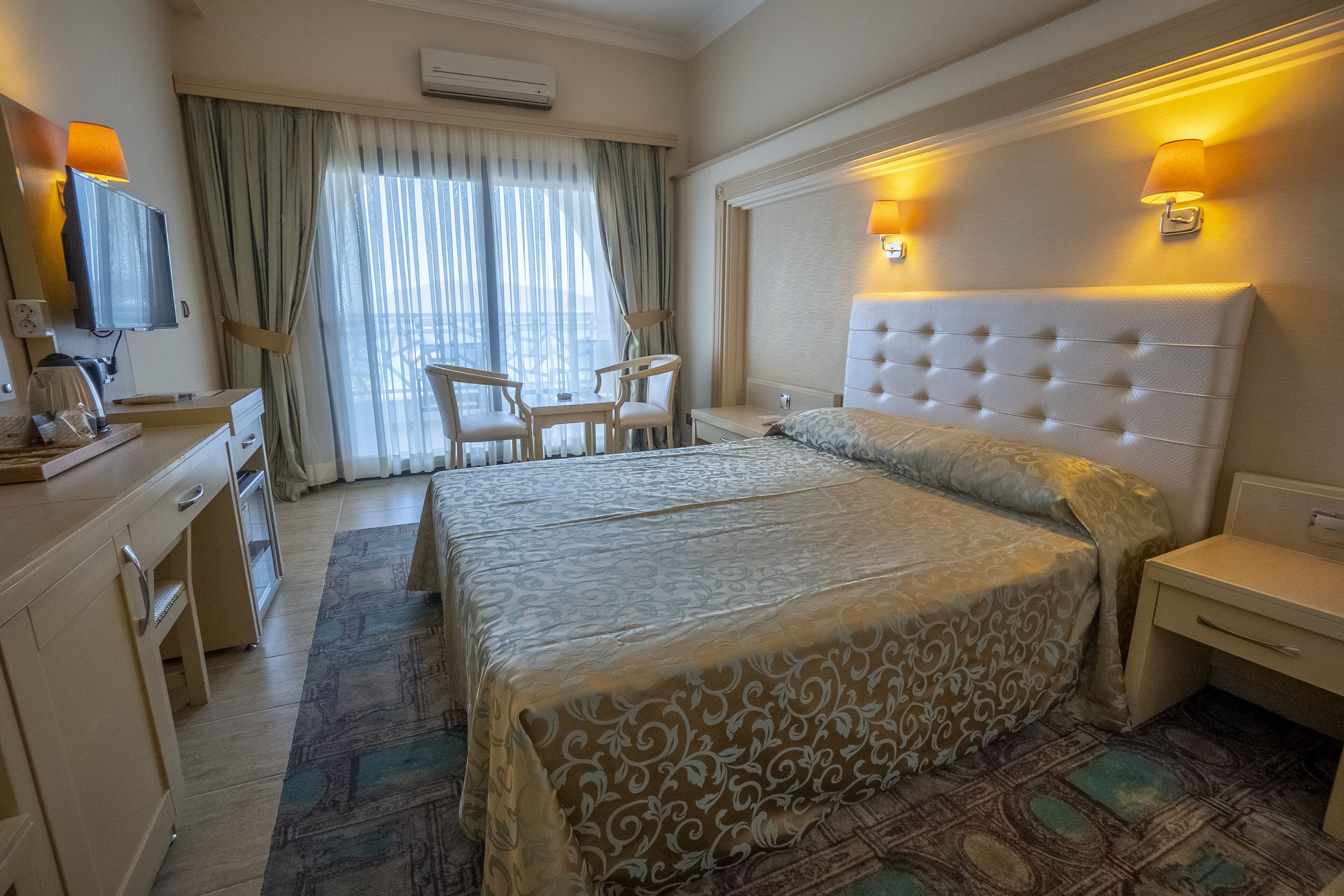 A hotel room with a large bed, a desk with a chair, a television, and a window with curtains.