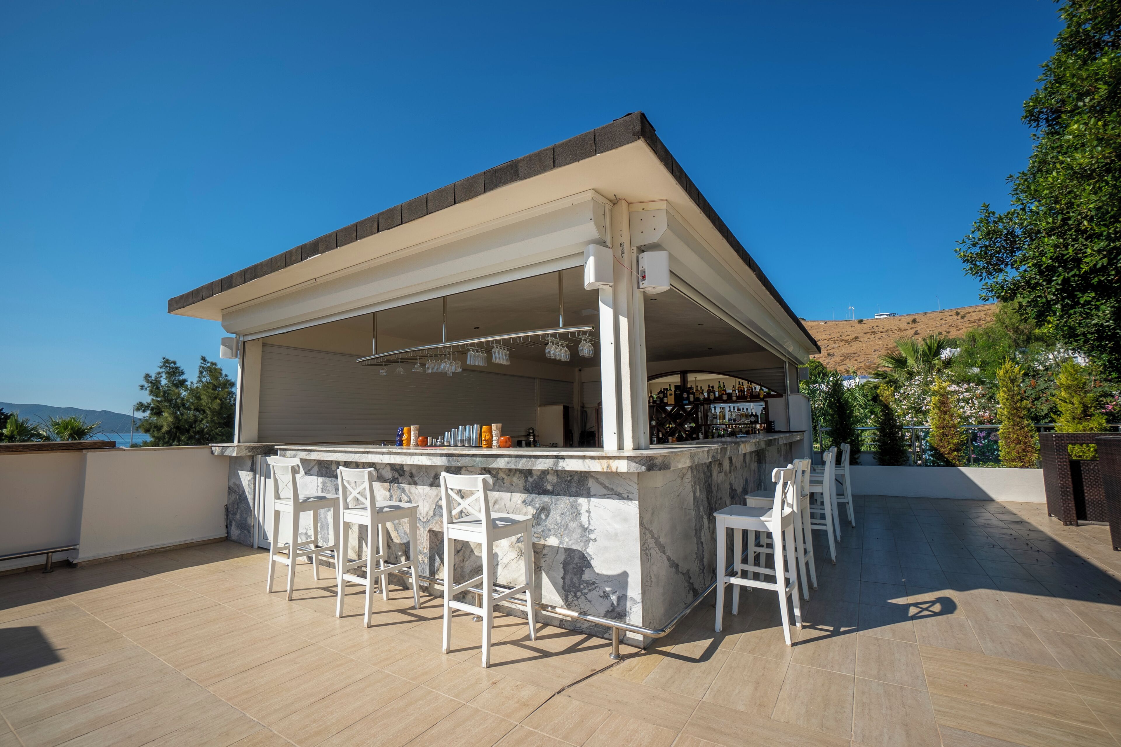 An outdoor bar area with a marble countertop, white bar stools, and a view of the landscape.