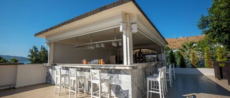 An outdoor bar area with a marble countertop, white bar stools, and a view of the landscape.