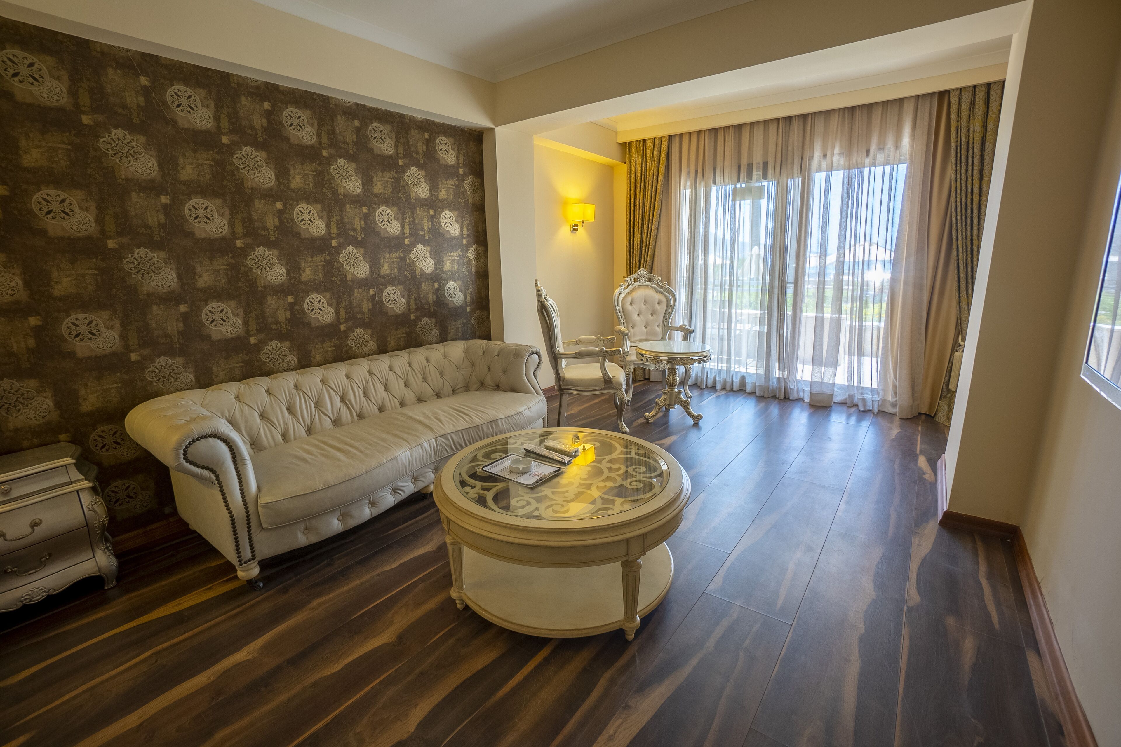 A living room with a beige sofa, a round coffee table, and a patterned wallpaper.