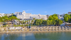 Un hotel frente a la playa con varios balcones, una zona de piscina y una playa con tumbonas.