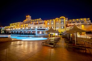 Un hôtel doté d’une piscine, d’un espace extérieur aménagé et d’une façade bien éclairée la nuit.
