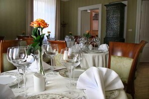 A dining table set with white tablecloths, glassware, and a vase with a single flower. - Ostoya Palace (Kraków)