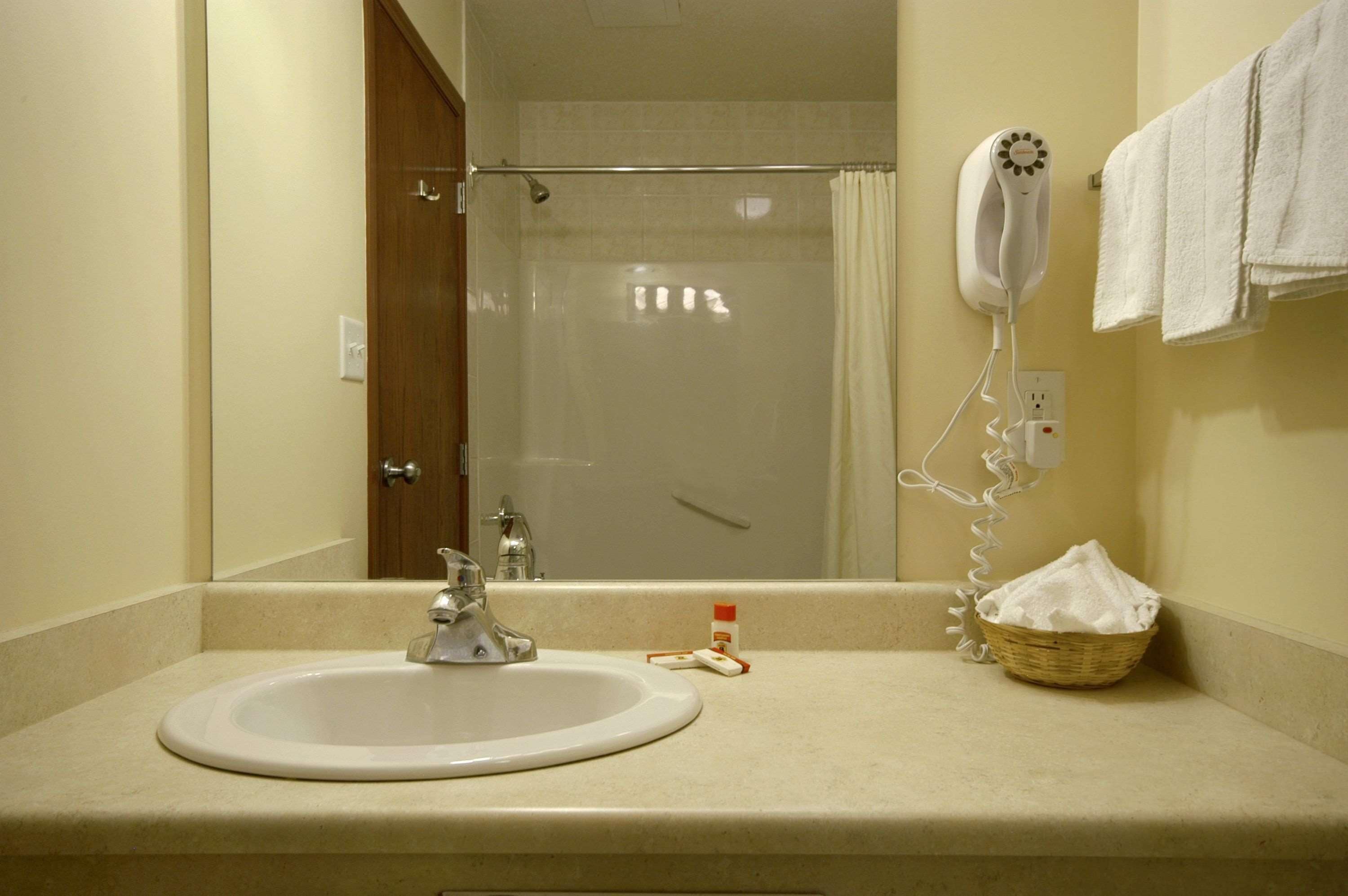 A bathroom with a sink, a hairdryer, and a basket of towels.