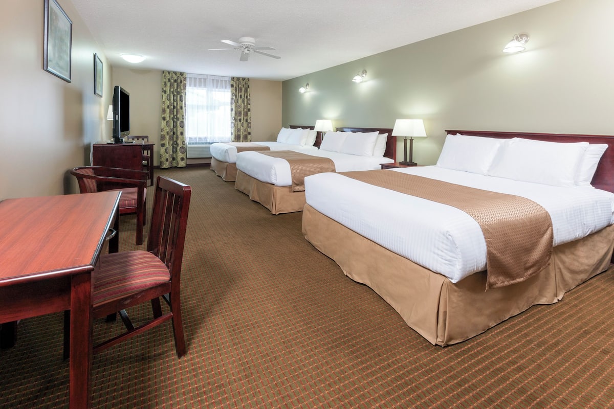 A hotel room with three beds, a desk, and chairs.