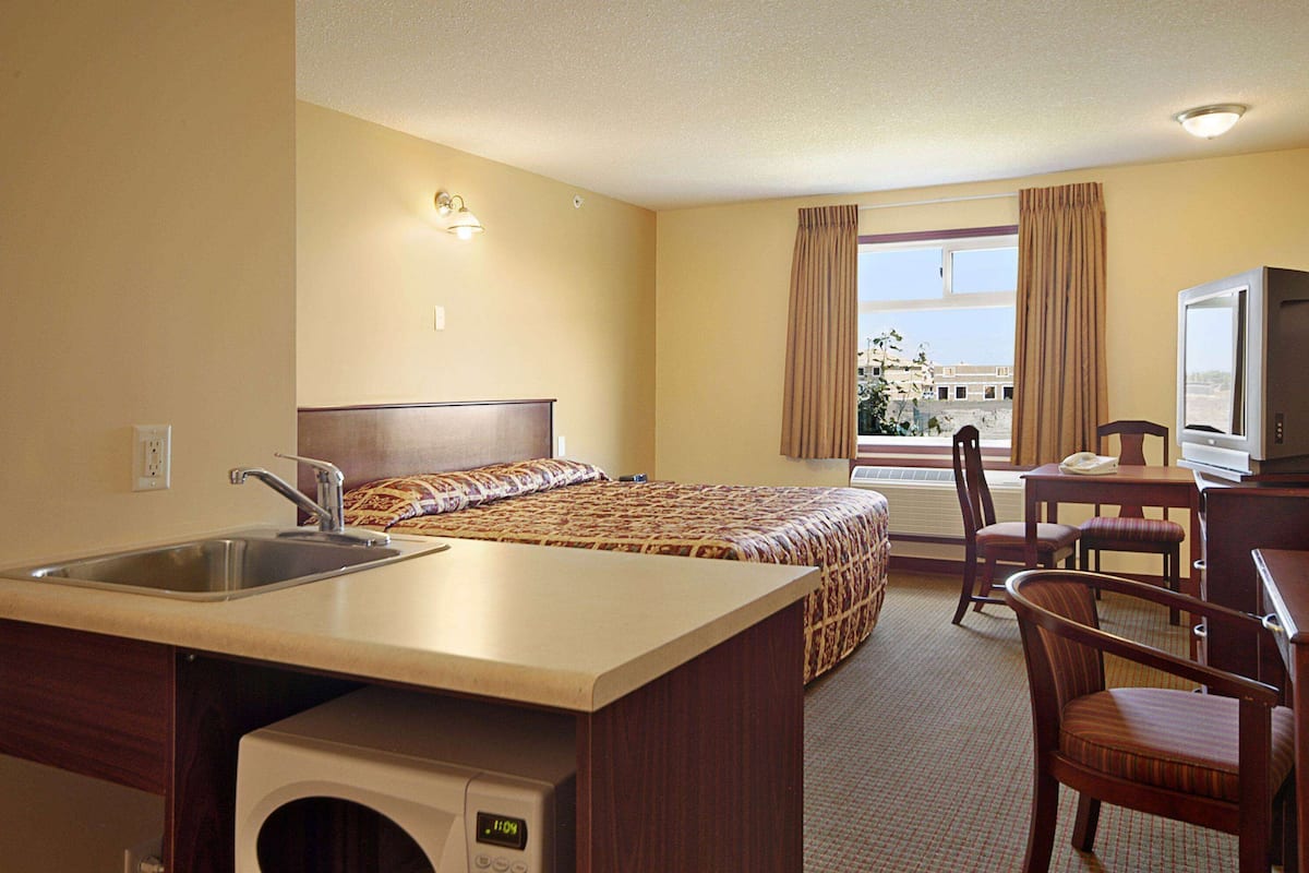 A hotel room with a bed, a desk with a chair, a television, a sink, and a window with curtains.