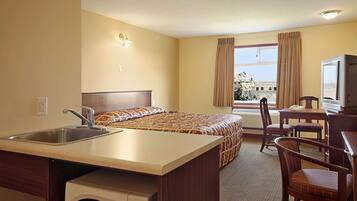 A hotel room with a bed, a desk with a chair, a television, a sink, and a window with curtains.