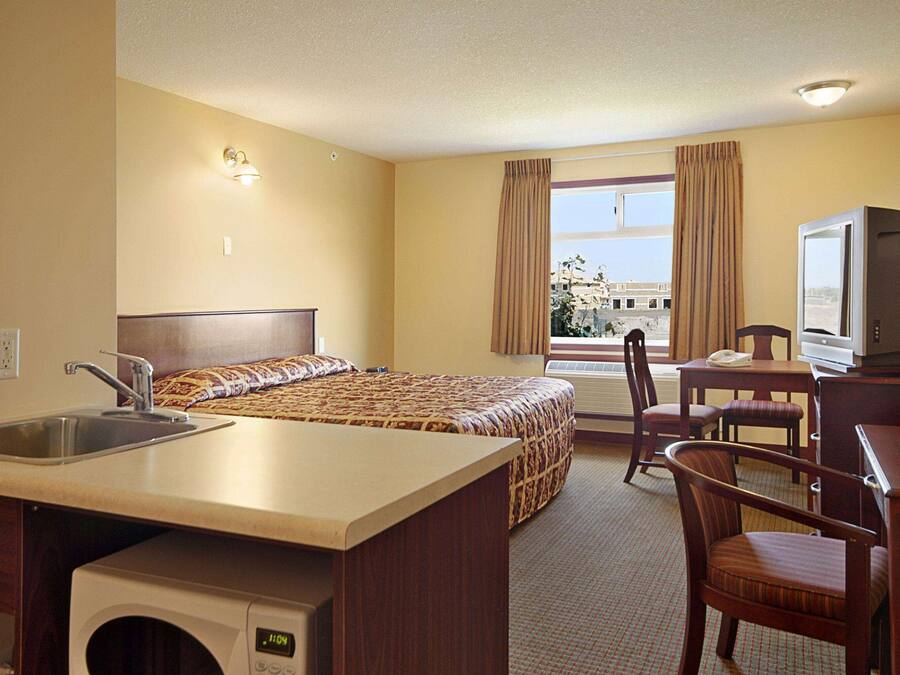 A hotel room with a bed, a desk with a chair, a television, a sink, and a window with curtains.