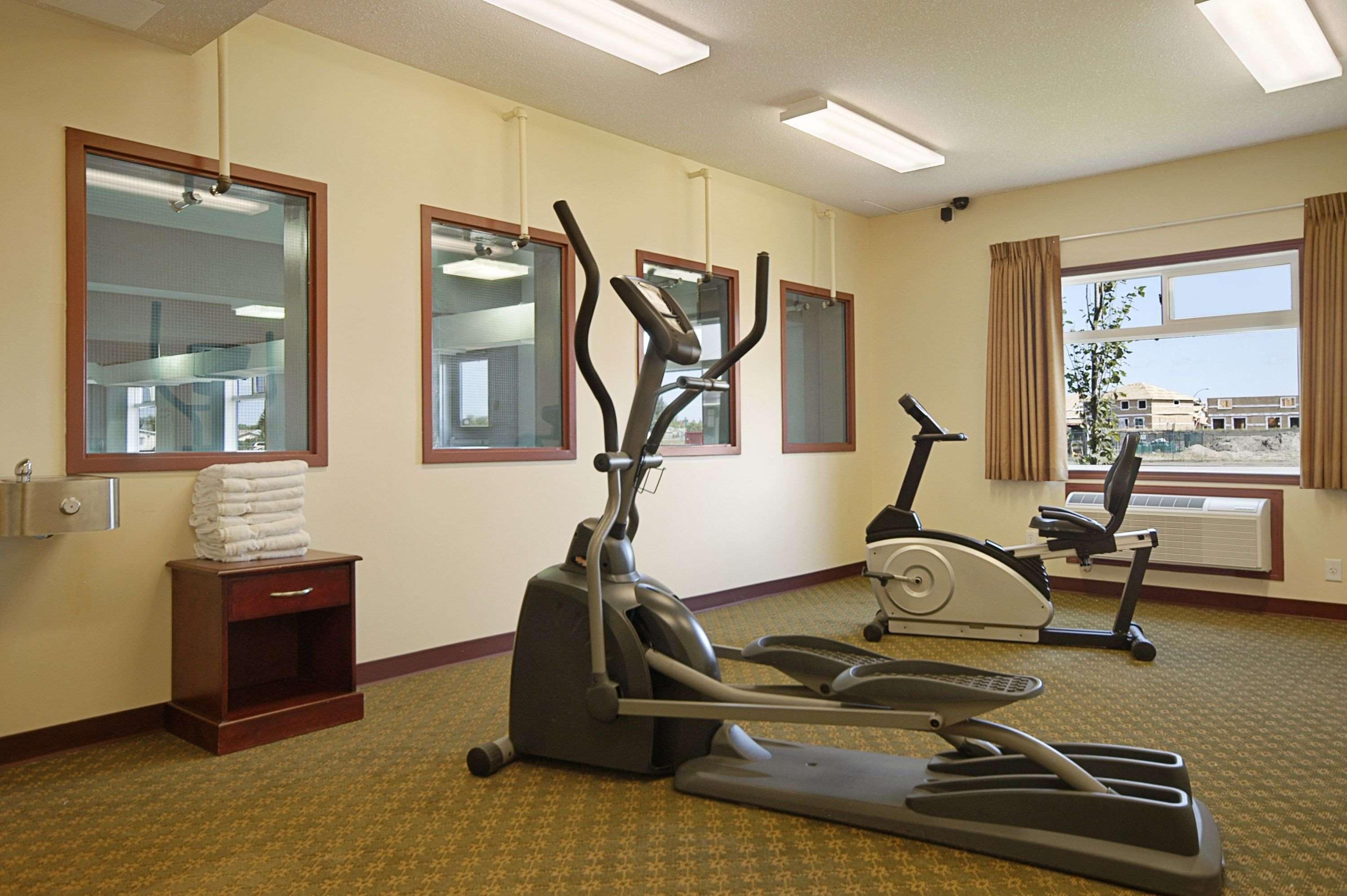 A hotel fitness room with exercise equipment, large windows, and a view of the outside.