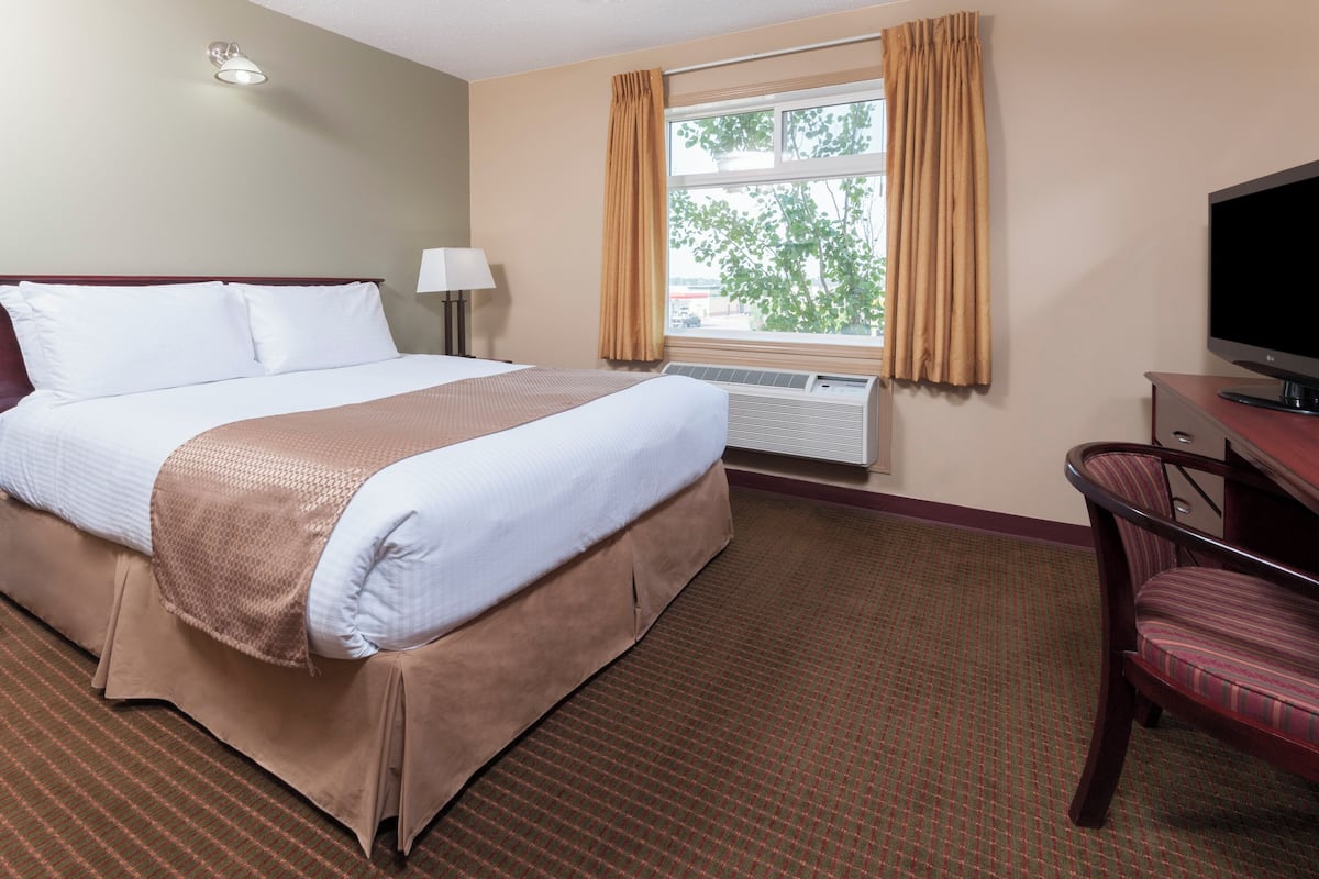 A hotel room with a large bed, a TV, a desk, and a window with curtains.