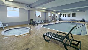 Una piscina interior con vistas claras al área de la piscina, que incluye un trampolín, sillas de descanso y un pequeño jacuzzi.
