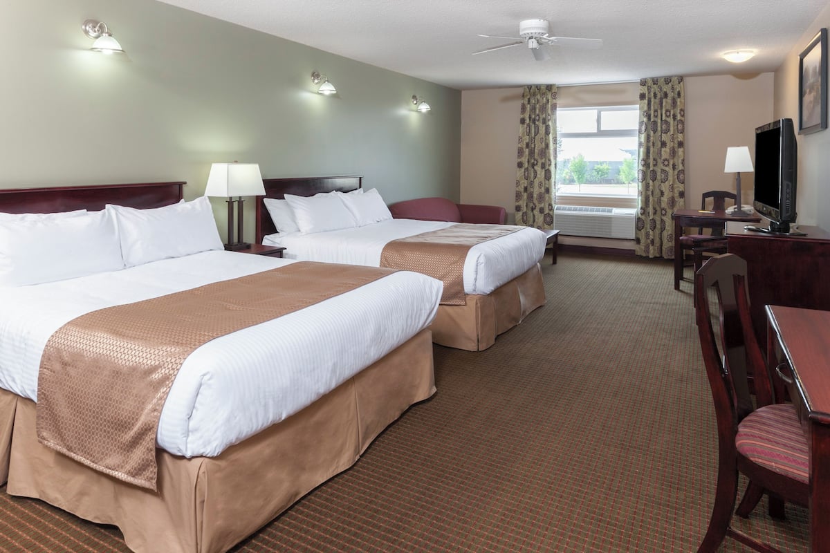 A hotel room with two beds, a desk, a chair, a television, and a window with curtains.
