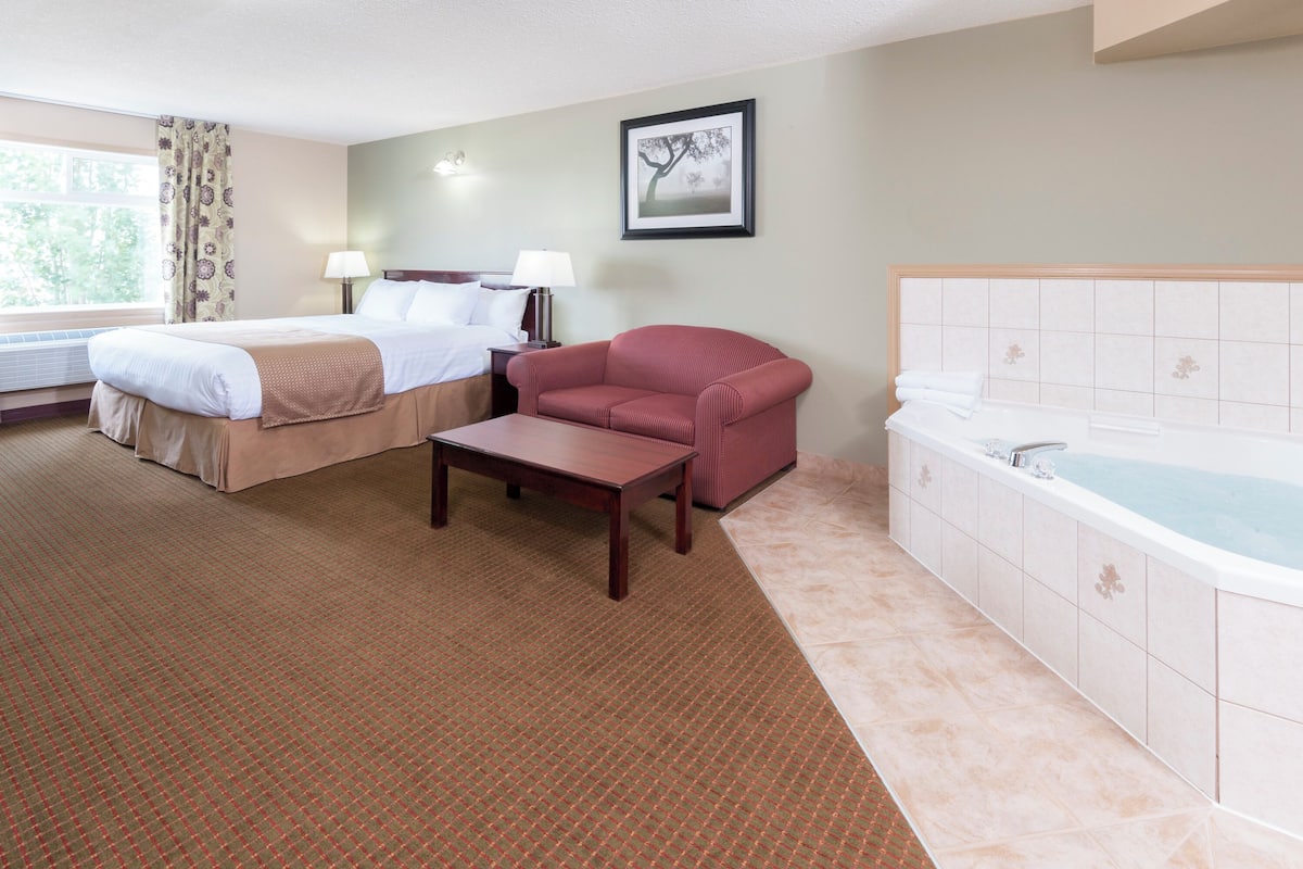 A hotel room with two beds, a red sofa, a small table, a bathtub, and a window with curtains.
