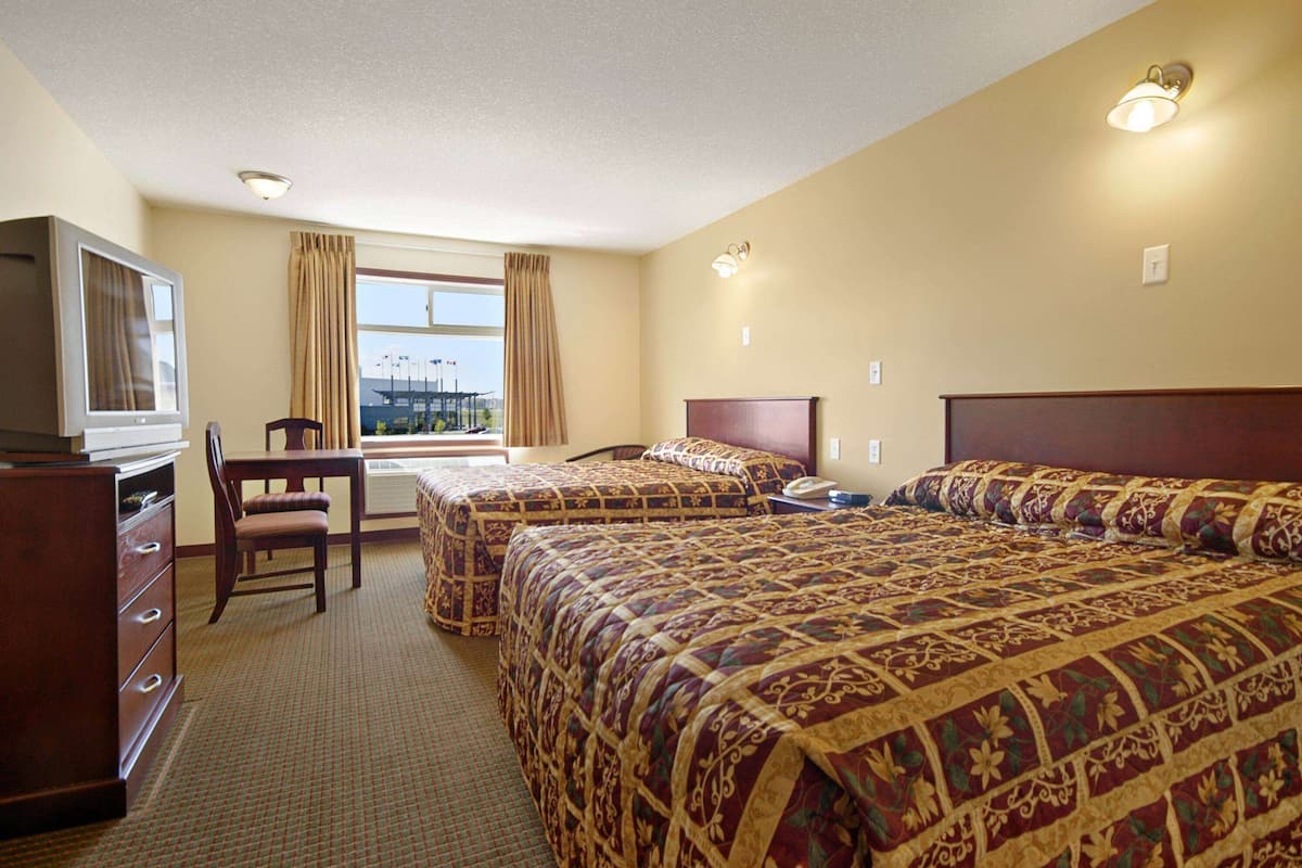 A hotel room with two beds, a desk, a chair, a television, and a window with curtains.