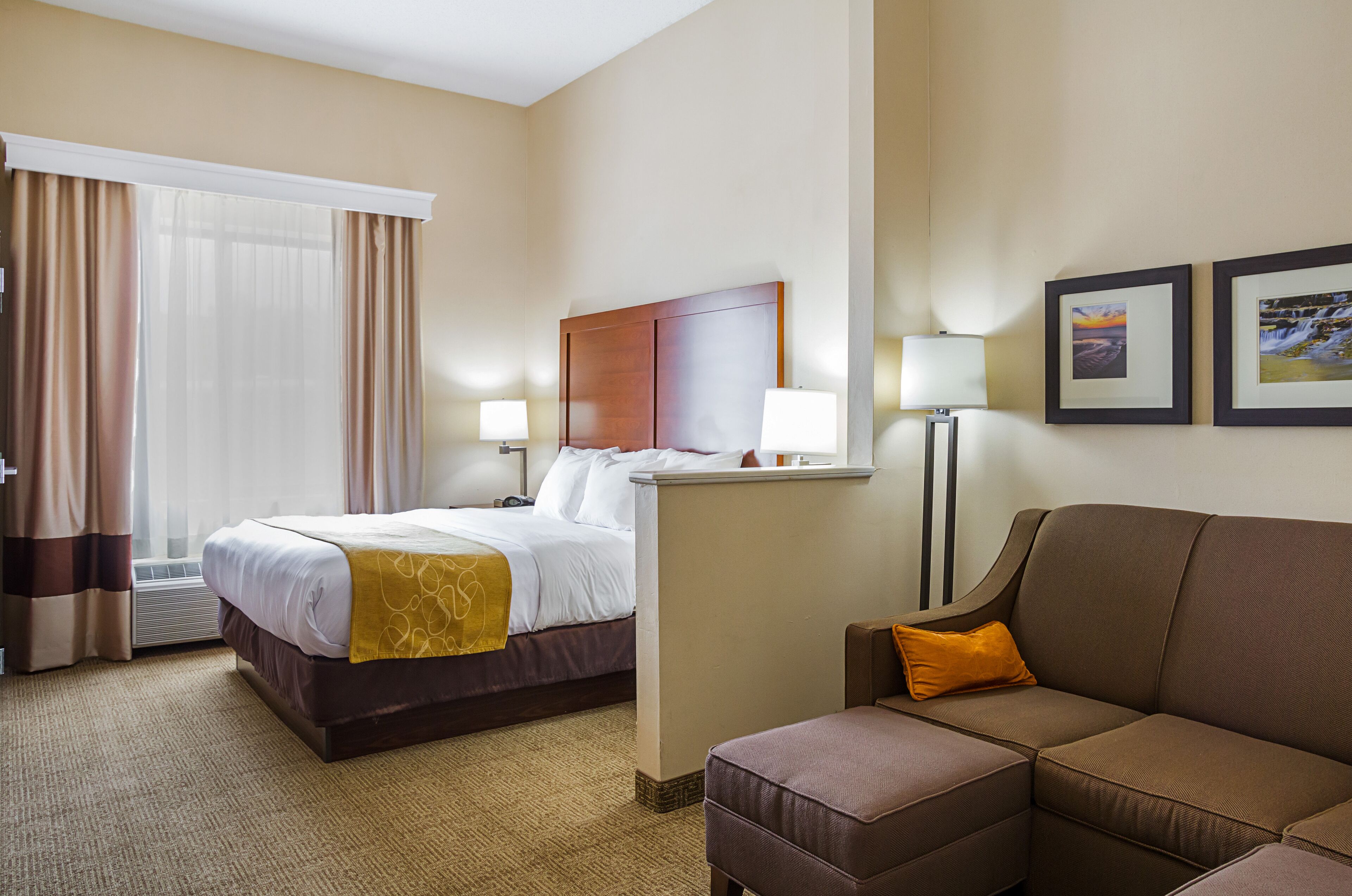 A hotel room with a bed, a sofa, a desk, and two lamps.