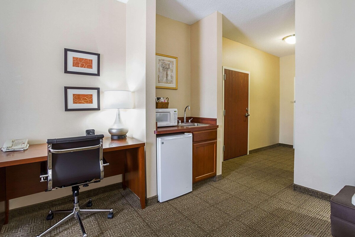 A hotel room with a desk, chair, microwave, refrigerator, sink, and two framed pictures on the wall.