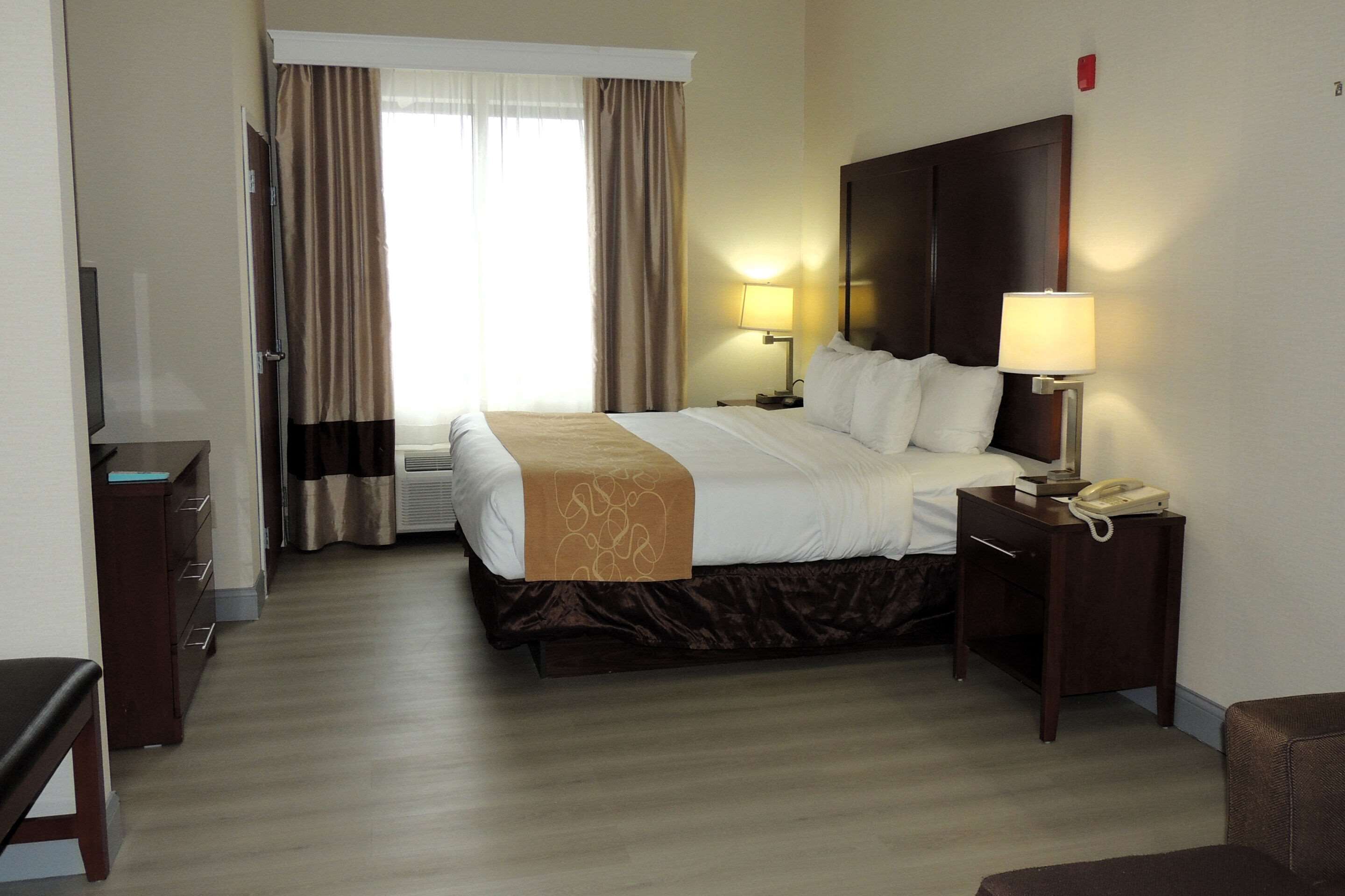 Habitación de hotel con cama, mesita de noche, lámpara y escritorio con teléfono.