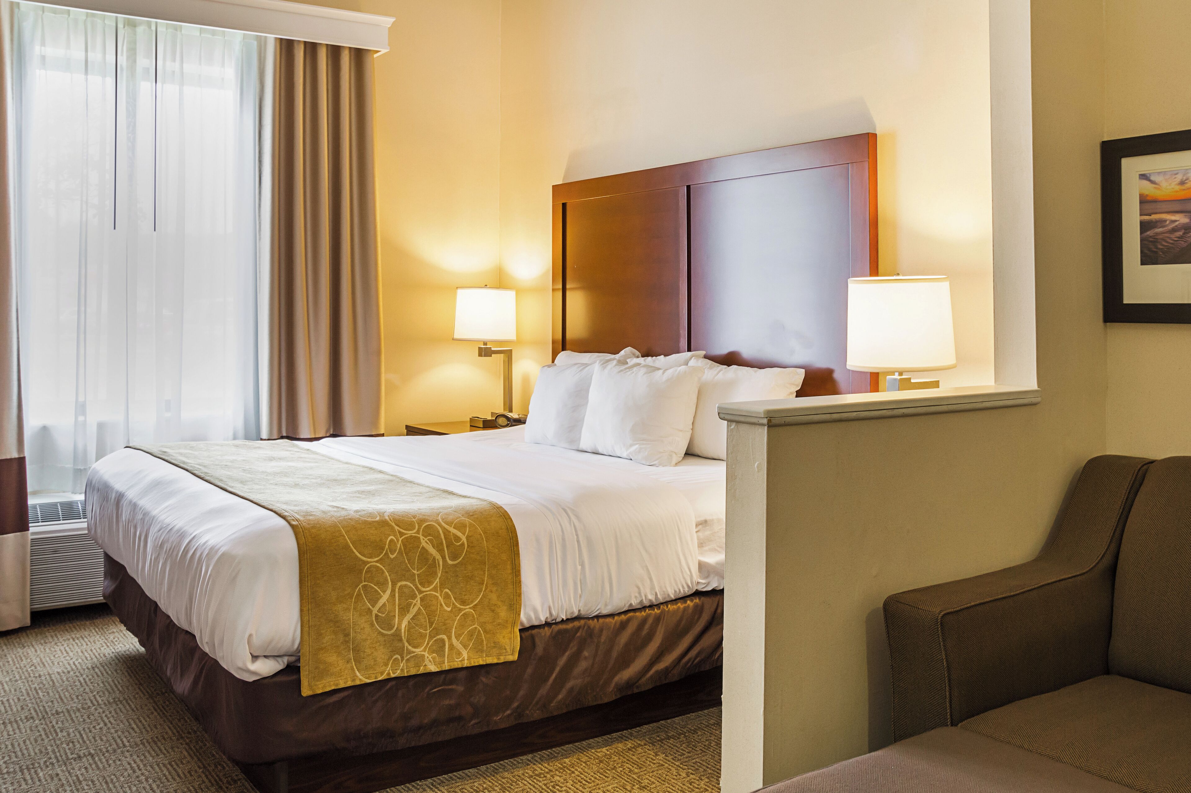 Une chambre d’hôtel avec un grand lit, deux lampes de chevet, une tête de lit, une fenêtre avec des rideaux et un tableau encadré au mur.