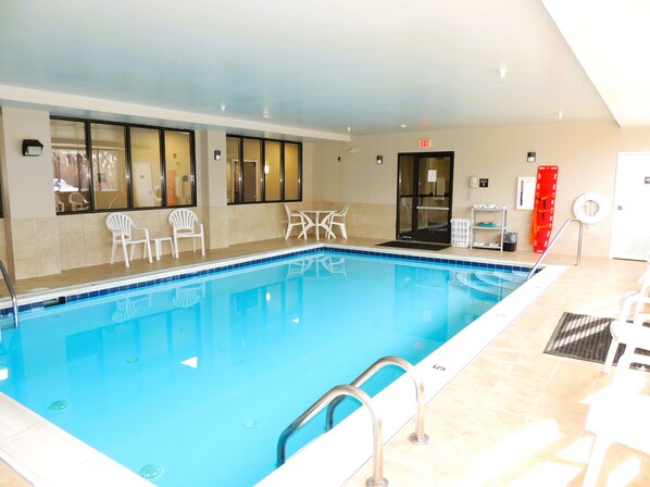 A swimming pool with a tiled edge, a metal ladder, and white plastic chairs.