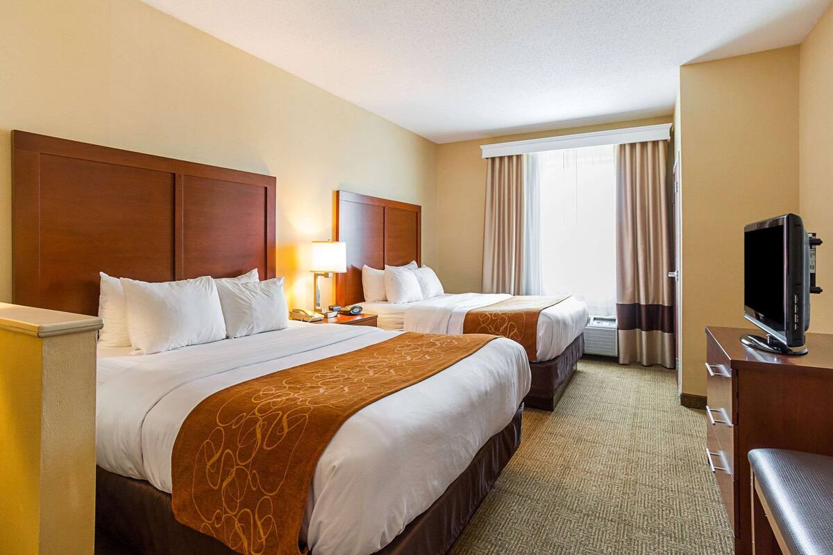 A hotel room with two beds, a television, and a large window with curtains.