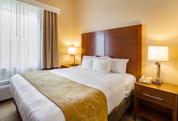 Une chambre d’hôtel avec un grand lit, une tête de lit en bois, deux tables de chevet avec des lampes, un téléphone et une fenêtre avec des rideaux.