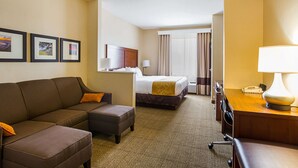 A hotel room with a bed, a sofa, an ottoman, a desk with a lamp, and framed pictures on the wall. - Comfort Suites Twinsburg (Twinsburg)