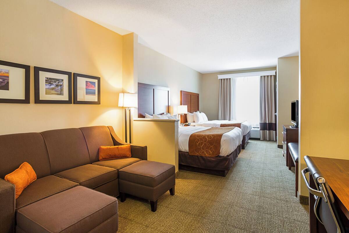 A hotel room with a sofa, a bed, a desk, and a television.