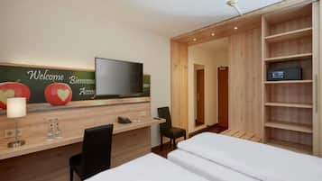 A hotel room with a bed, a desk with a chair, a TV, and a wardrobe.