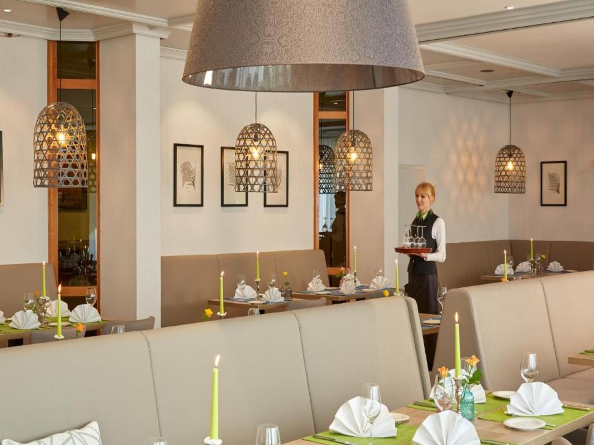 Interior de restaurante con cabinas, lámparas colgantes y un camarero atendiendo.