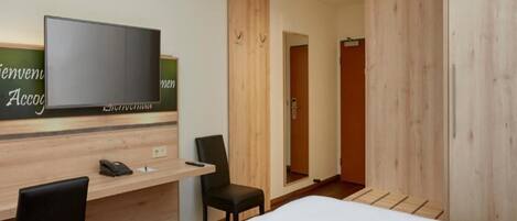 Una habitación de hotel con escritorio de madera, televisor, cama y espejo.