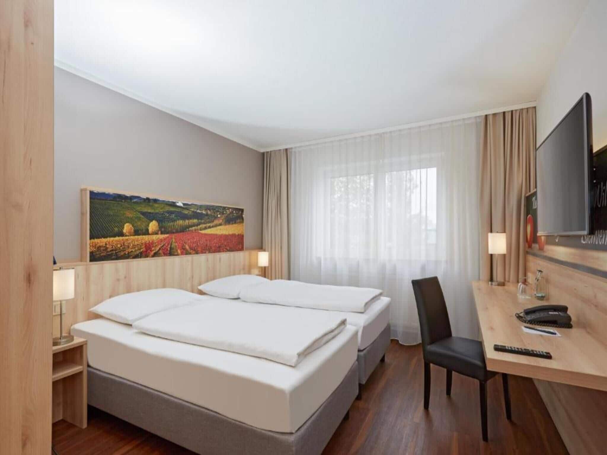 Ein Hotelzimmer mit zwei Betten, einem Schreibtisch mit Stuhl, einem Fernseher und einem Bild an der Wand.