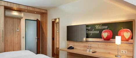 A hotel room with two beds, a wooden wall, a welcome sign, and a small desk with a phone and glasses.