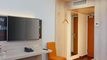 A hotel room with a bed, a desk with a telephone, a chair, and a television mounted on the wall.
