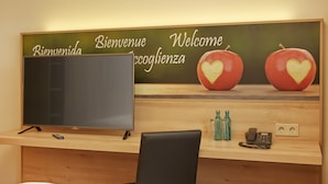 Ein Hotelrezeptionsschalter mit Fernseher, einer Holztresen, einem schwarzen Stuhl und einem Willkommensschild mit Äpfeln.