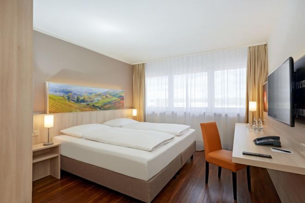 Ein Hotelzimmer mit zwei Betten, einem Schreibtisch mit Stuhl, einem Fernseher und einem Bild an der Wand.